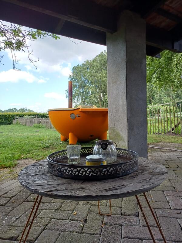 Oranje Dutchtub in de tuin, gezien vanonder een overkapping met een salontafel