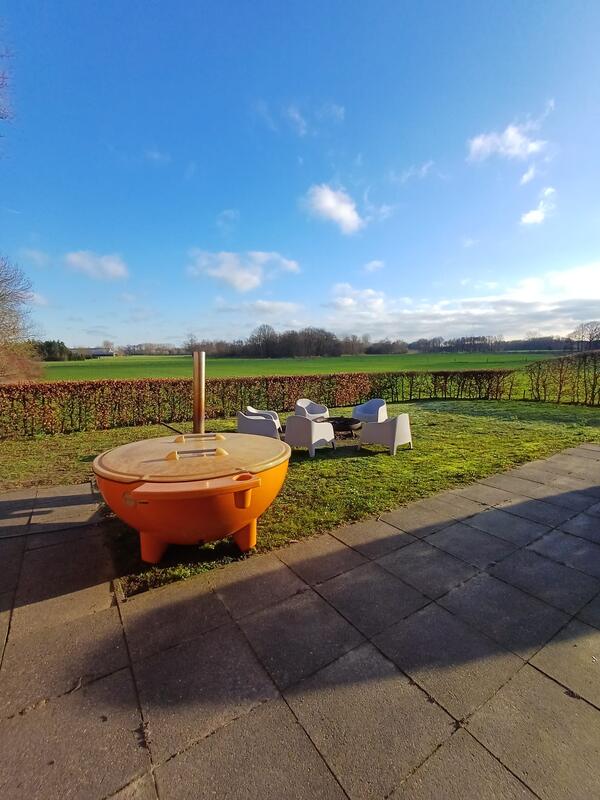 Oranje Dutchtub op het gras, met tuinstoelen rond een vuurschaal en uitzicht over de weilanden